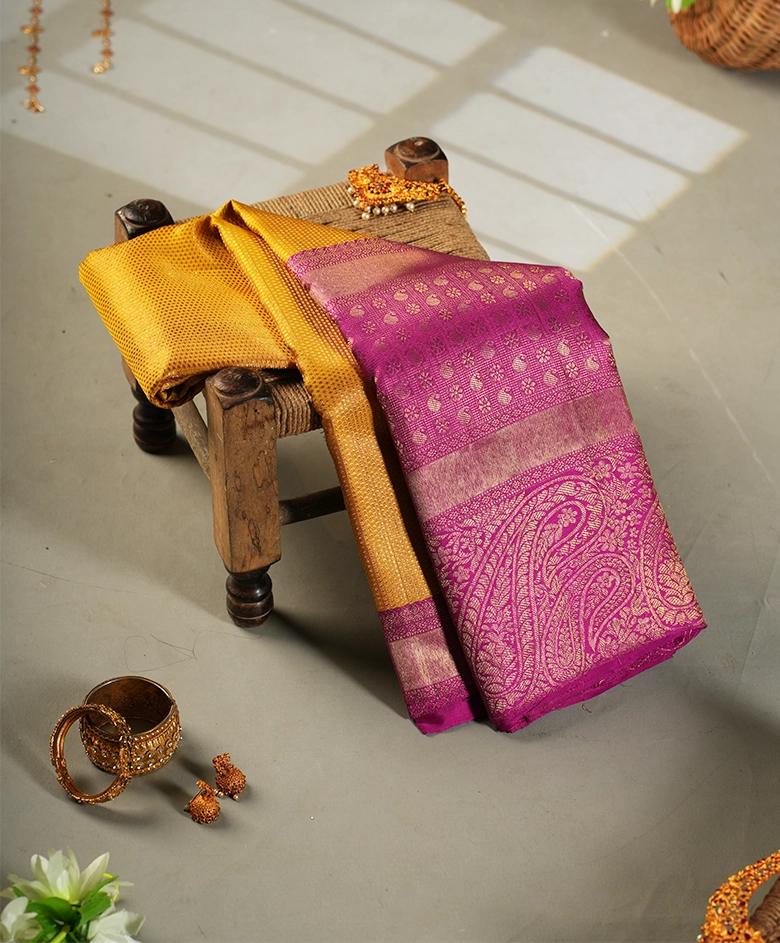 Traditional pink and gold silk saree with intricate patterns displayed on a wooden stool with jewelry.