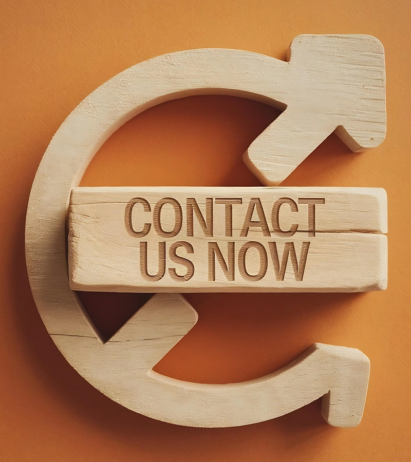 A wooden block with "CONTACT US NOW" engraved on it, placed over a wooden circular arrow symbol on a warm orange background.