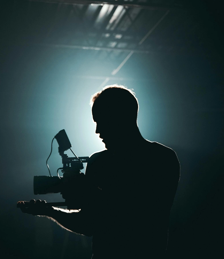 Silhouette of a videographer holding a professional camera with dramatic backlighting.